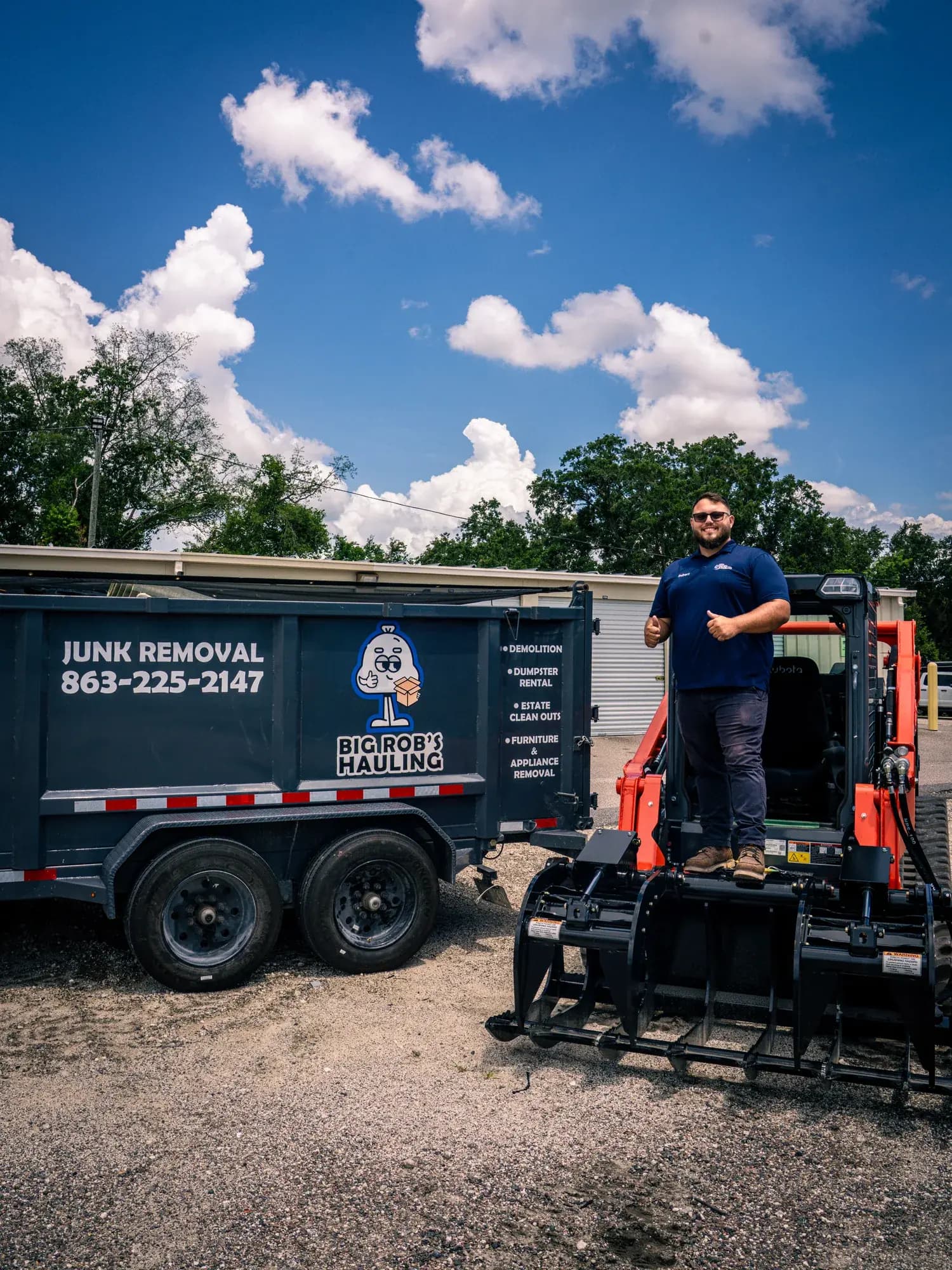 Rob of Big Rob's Hauling standing on the skid steer grapple beside a Junk Removal dump trailer in Davenport, FL